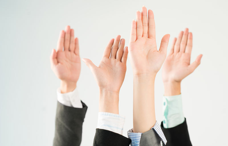 An image of four people wearing business shirts and suits raising their hand. 