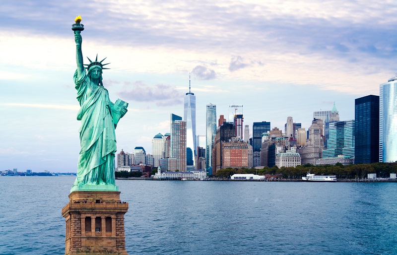 image of new york city with the Statue of Liberty to the left foreground of the image and new york harbour and skyscrappers in the background. 